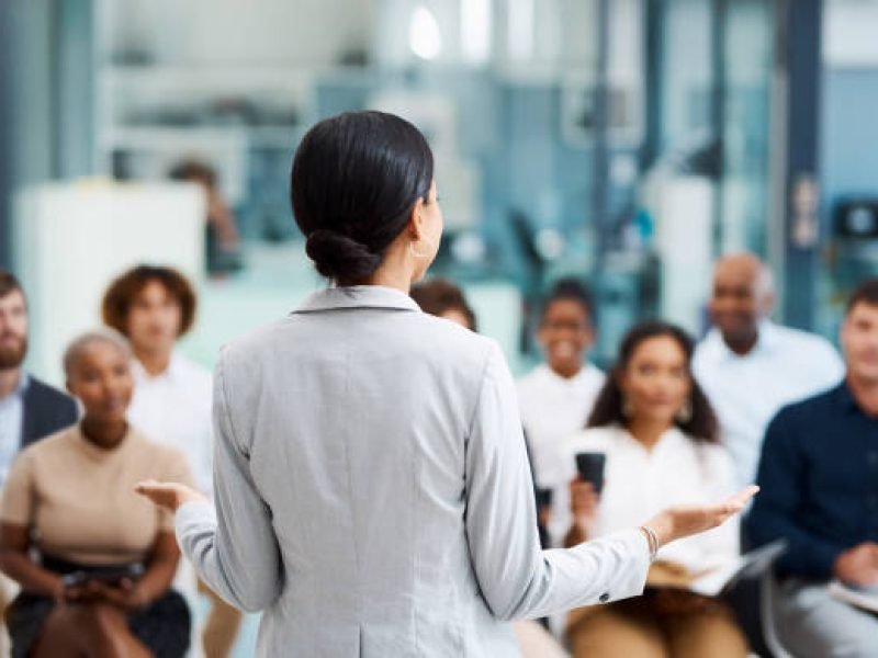 istockphoto-1312139041-612×612 Rearview shot of an unrecognizable businesswoman giving a presentation in the office boardroom